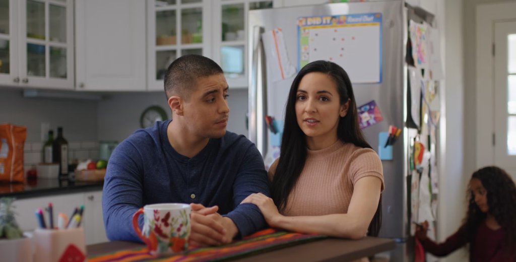 A woman and a man holding arms at a table in their kitchen